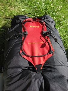 Côté avant du sac avec des porte-matériel et le cordon élastique situé sur la poche rouge ouverte (poche à crampon par exemple)