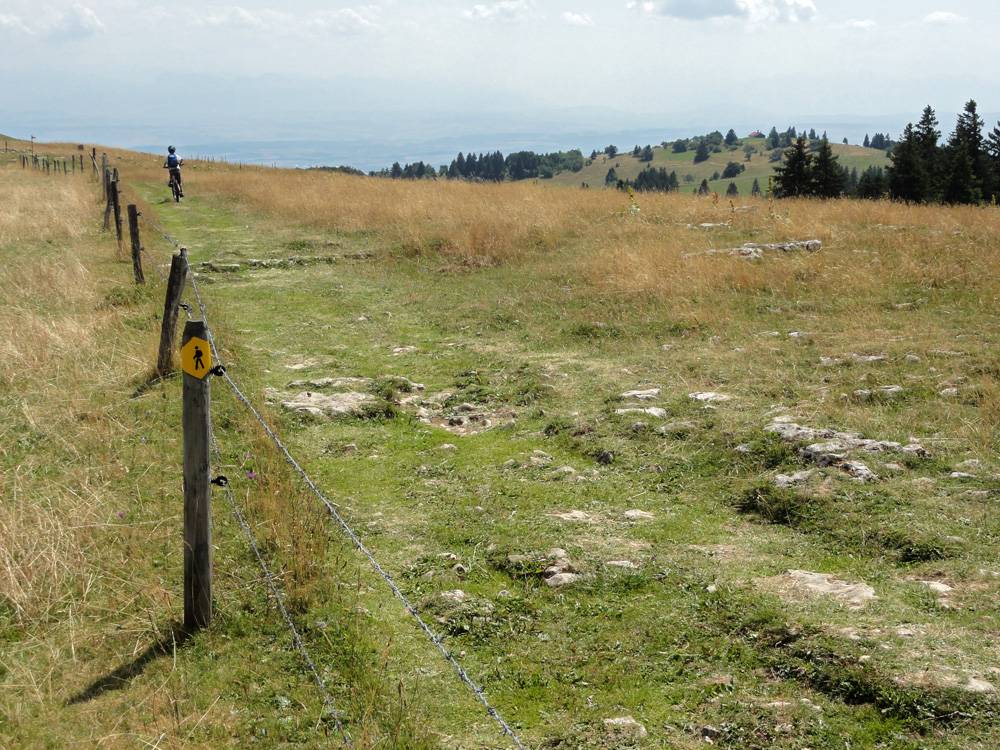 Le Creux du Van se visitera en mode piéton et se franchira en mode VTT. Première clôture à "camber" avec véhicules et bagages. Au fond à droite l’œil averti distinguera la cabane Perrenoud sur sa colline, l'objectif du soir.