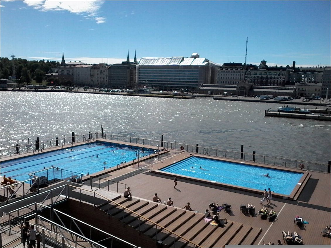 Je suis montée sur un bâtiment en bois (terrasses et cafés) qui surplombe le port. Juste en dessous se trouvent les piscines. Et aussi plus à droite, un cours de sieste. Chacun est allongé sur un petit tapis et un gars déambule en tapotant un tambour. Finalement, c'est peut être une séance intensive de stretching finlandais.