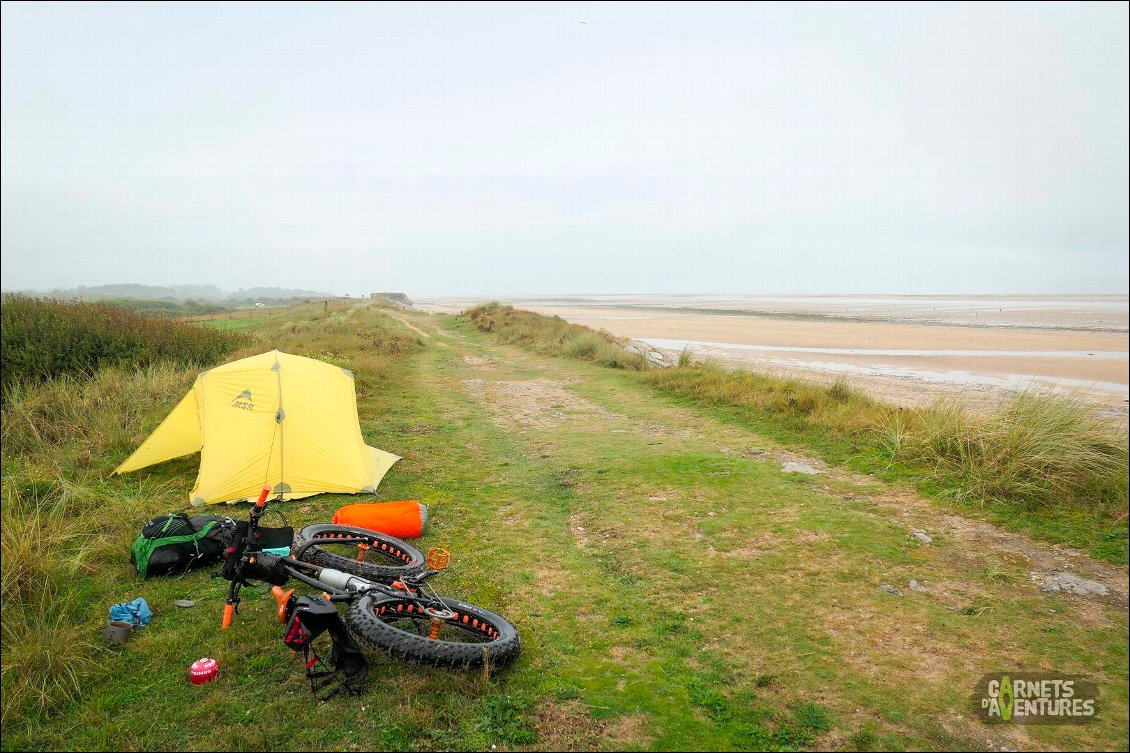 Le bivouac au matin. Atmosphère relativement humide.
La veille au soir, un peu présomptueux, j'ai estimé que le coefficient de marée était assez faible pour dormir tout en haut de la plage. En pleine nuit, je suis pris d'un doute : et si la houle était plus forte que prévue ? Sous l'abri, l'invasion de puce de mer qui viennent jusque dans mon cou finit de me décider : je déménage. Il est 1h30 du matin !
La nuit se termine bien plus agréablement...